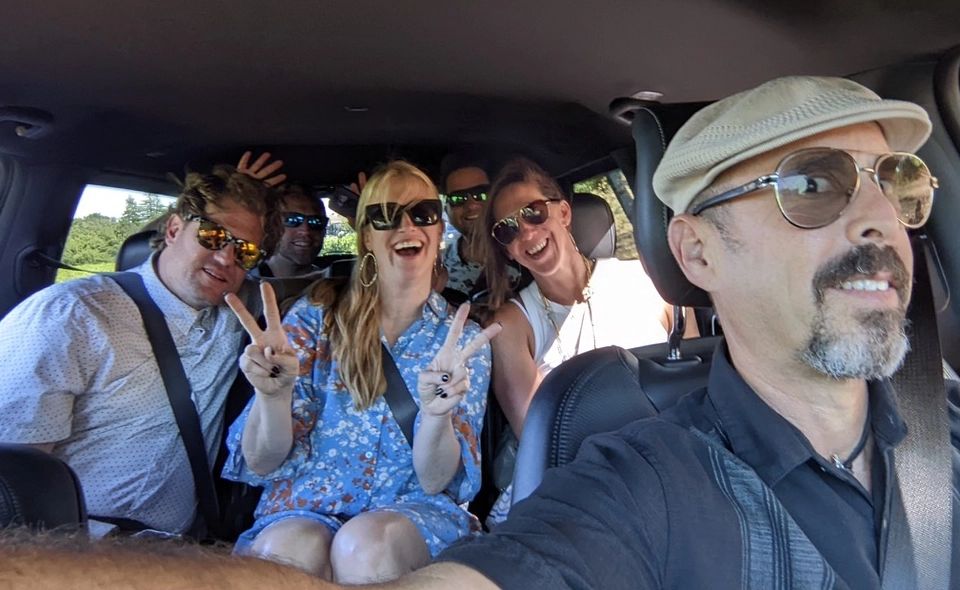 Driver and wine tour guests smiling and flashing peace signs inside a vehicle on the way to Monterey County wineries