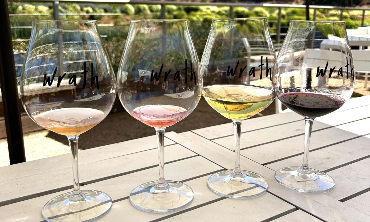Flight of four wine glasses holding orange, rosé, white and red wine on a patio table at a Monterey County winery