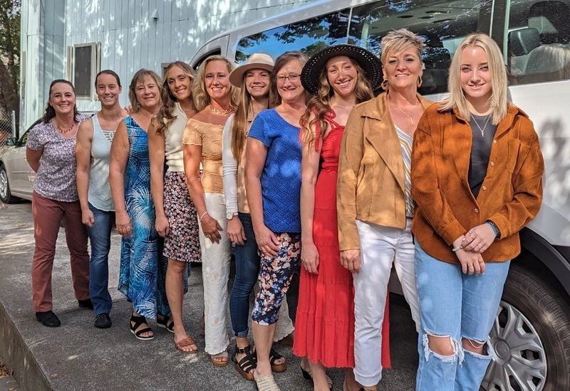 Row of nine smiling wine tour guests standing together beside a white passenger van in Plymouth, Amador County